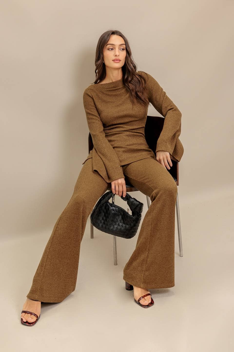 Woman in a brown outfit sitting on a chair against a beige background