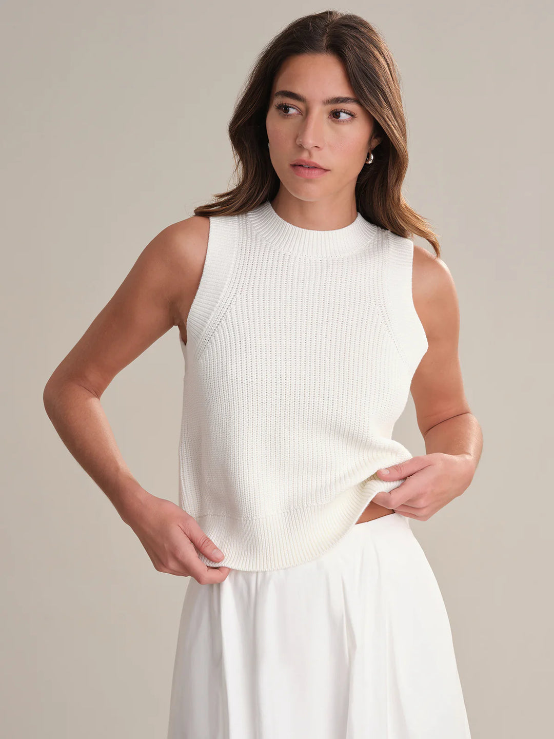 Woman wearing a white sleeveless top and skirt against a neutral background