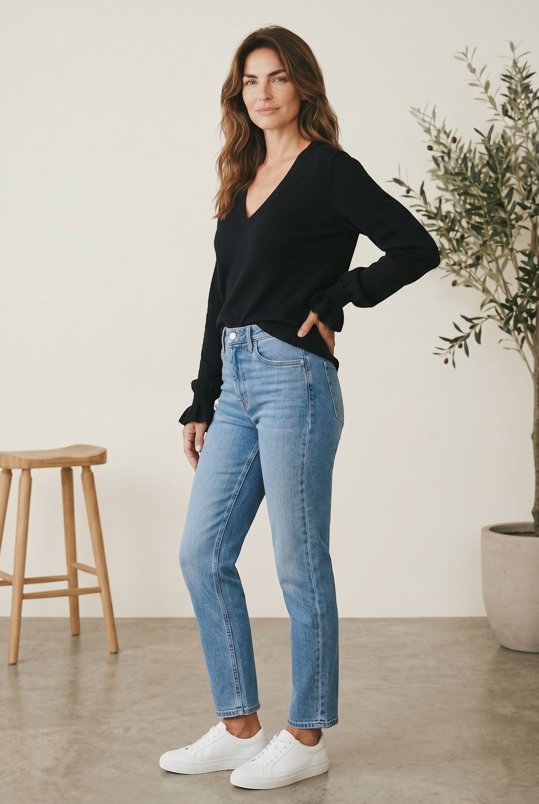 CAL JUNE black knit V-neck top with ruffle detail on cuffs, paired with light wash denim jeans.