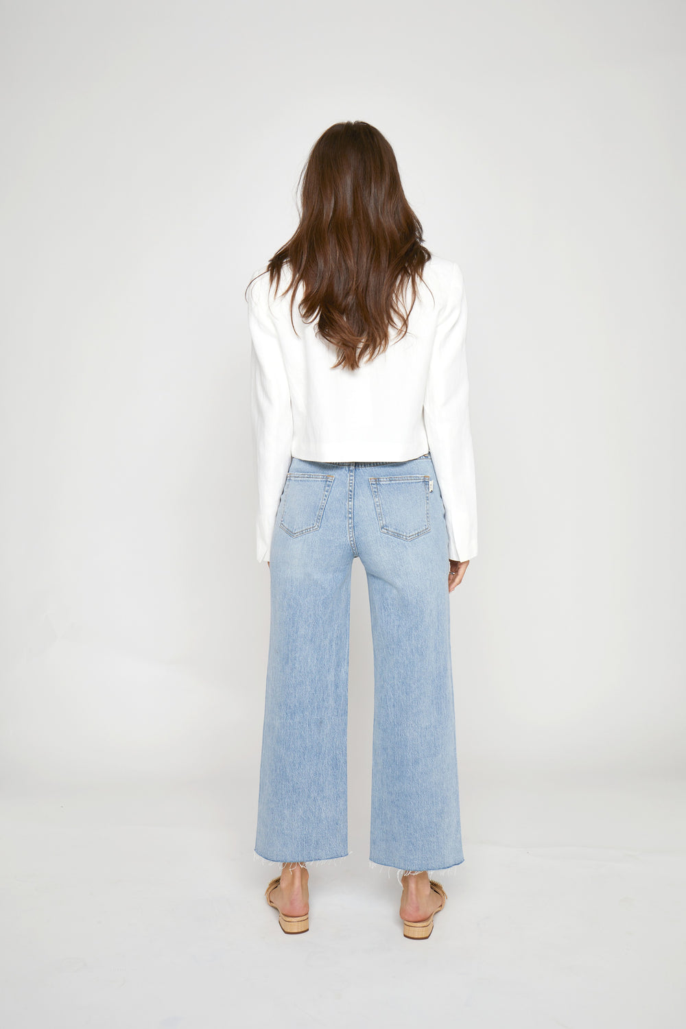 CAL JUNE light indigo worn wash high-rise wide leg cropped jeans with raw hem on a model.