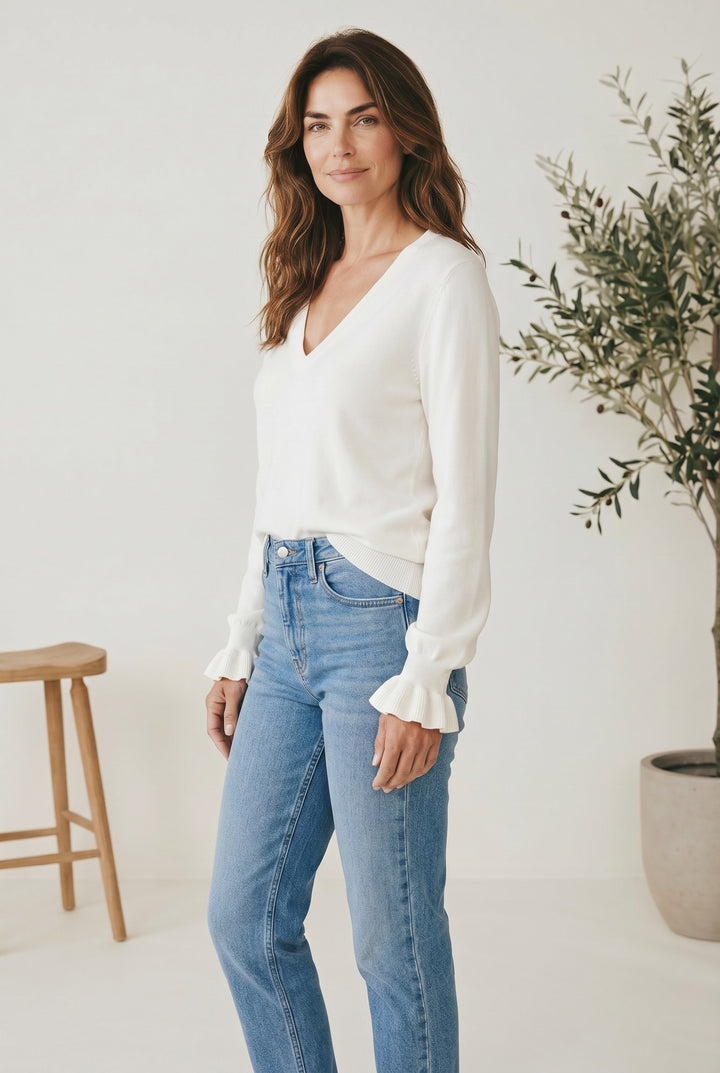 CAL JUNE The Louvre Ruffle Knit Top in cream, a V-neck sweater with ruffled cuffs, worn by a model with blue jeans.
