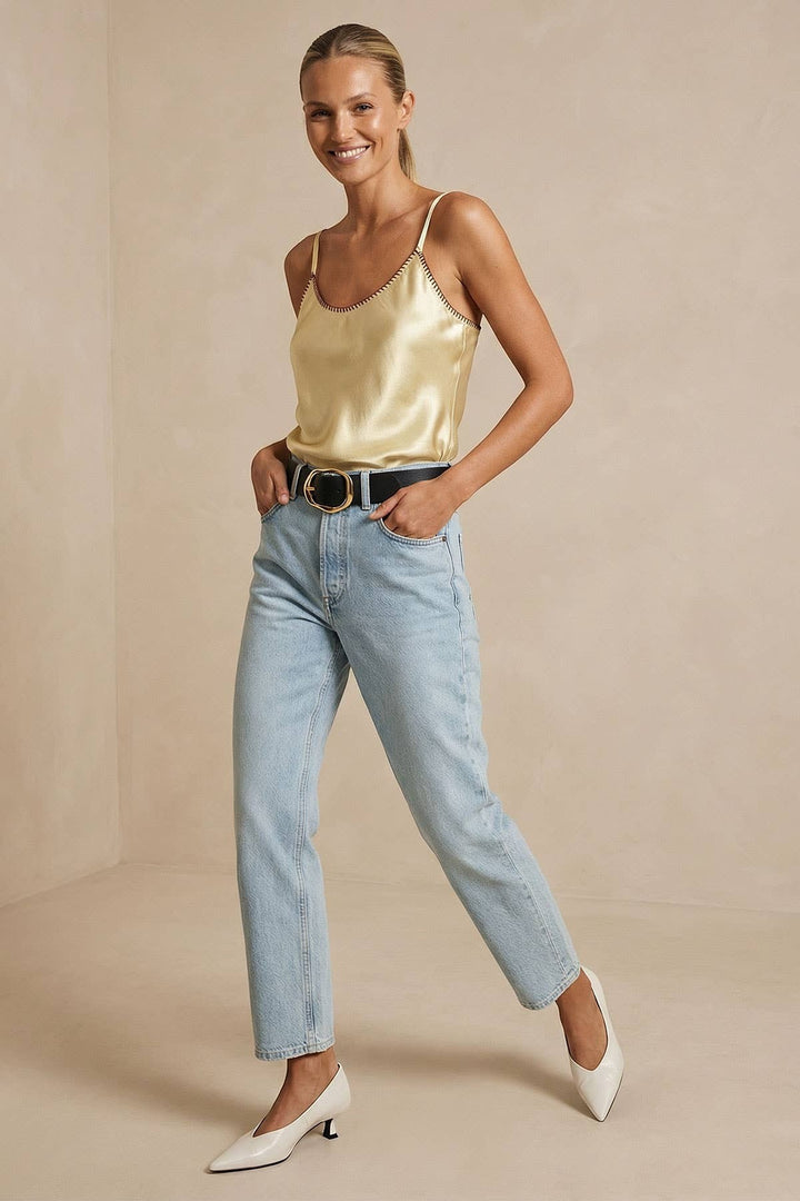 CAL JUNE pale yellow satin camisole top with whipstitch trim and adjustable straps, worn by a model with light wash jeans.