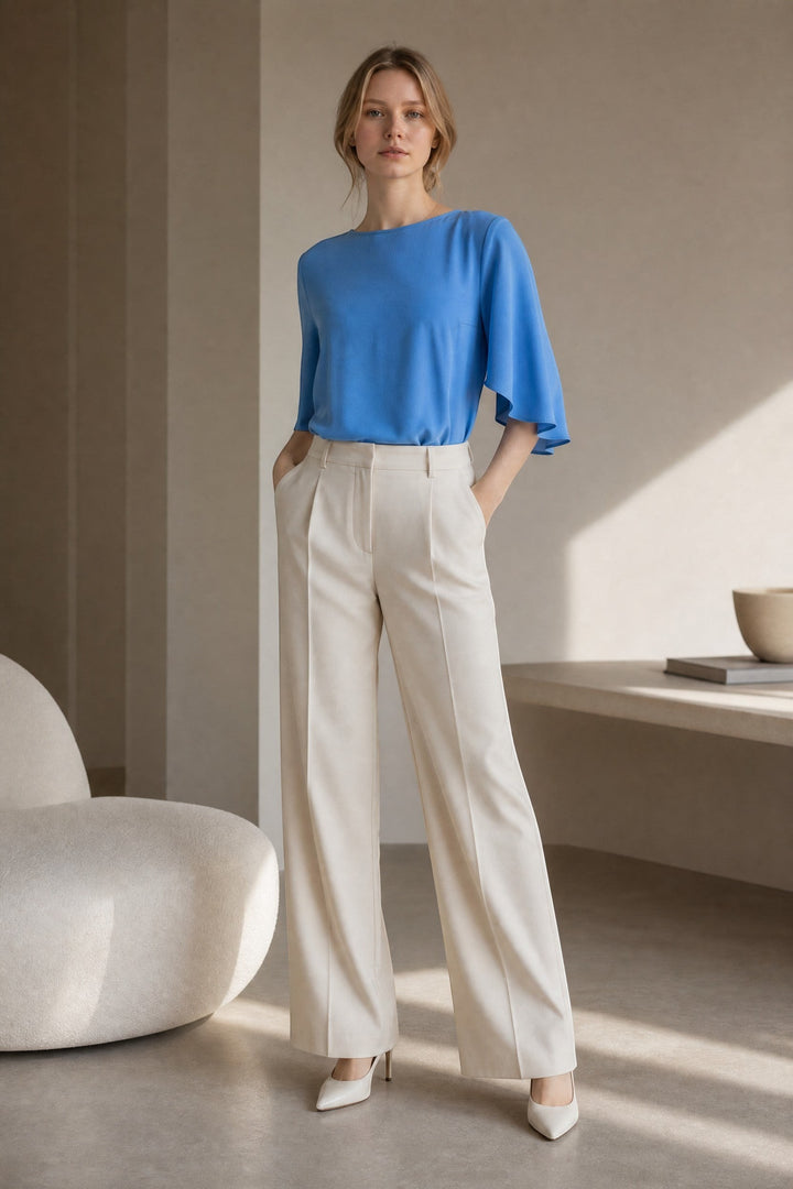 CAL JUNE The Marais Blouse in bright blue, a refined and feminine top with flutter sleeves, paired with cream wide-leg trousers.
