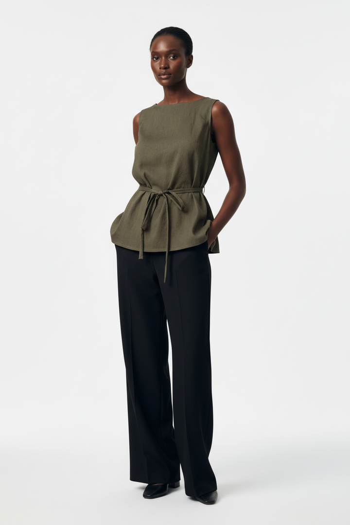 Model wearing a CAL JUNE olive sleeveless cinched tunic top with a boat neckline and waist tie, paired with trousers.