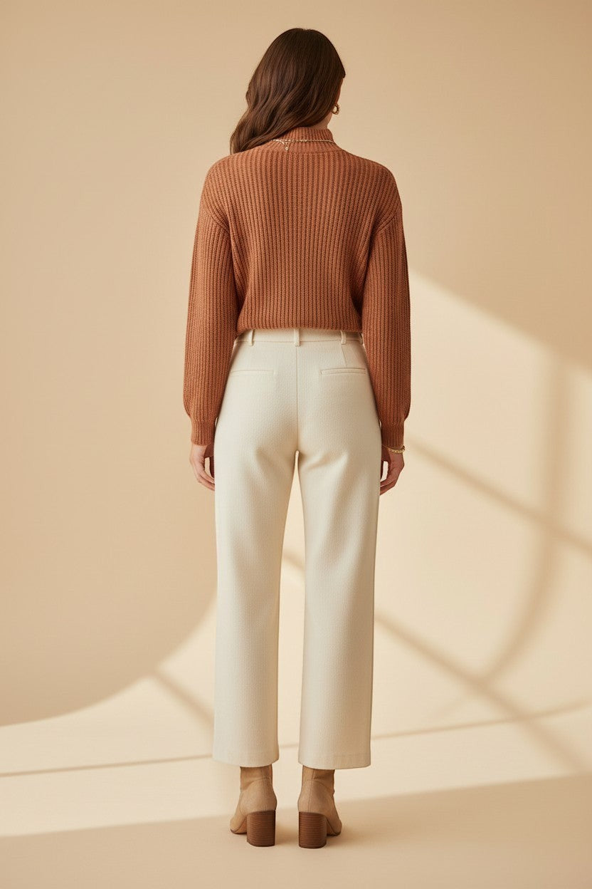 CAL JUNE rust-colored ribbed knit sweater with mock neck and ruffle detail on a model wearing cream trousers.