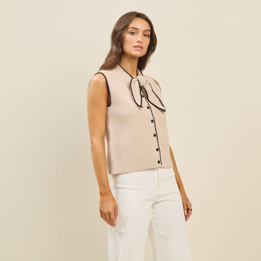 CAL JUNE Sienne sweater vest in beige knit with black whipstitch trim and bow detail. Model wears size S.