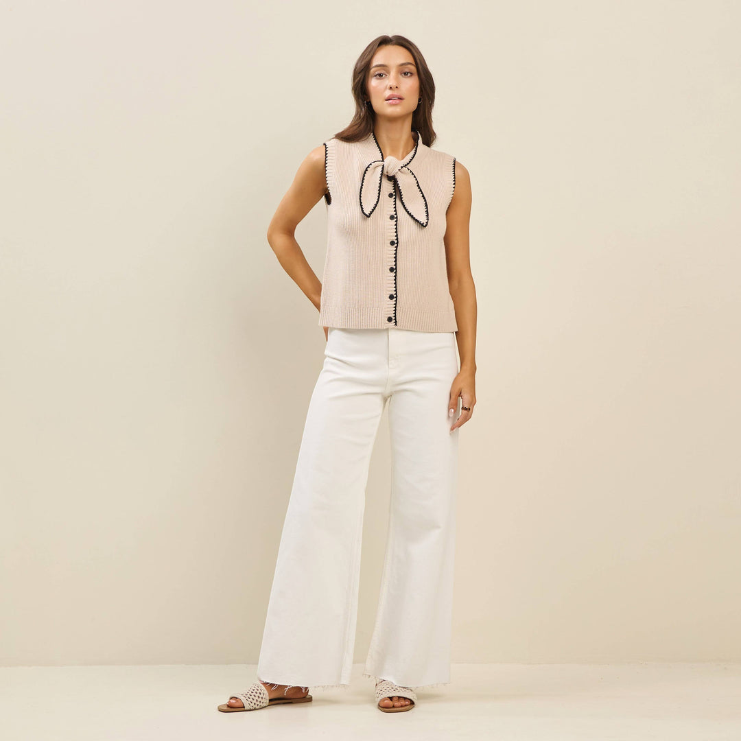 CAL JUNE The Sienne Whipstitch Sweater Vest in beige knit with black trim and bow detail. Model wears size S.