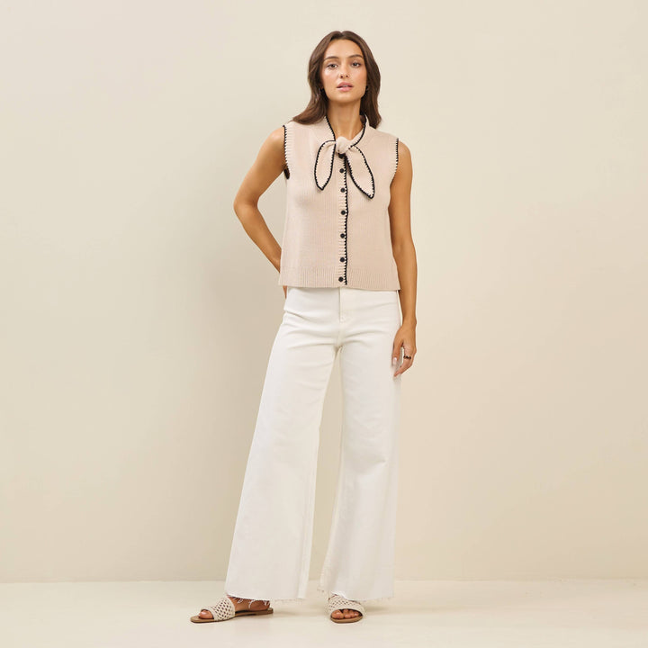 CAL JUNE The Sienne Whipstitch Sweater Vest in beige knit with black trim and bow detail. Model wears size S.