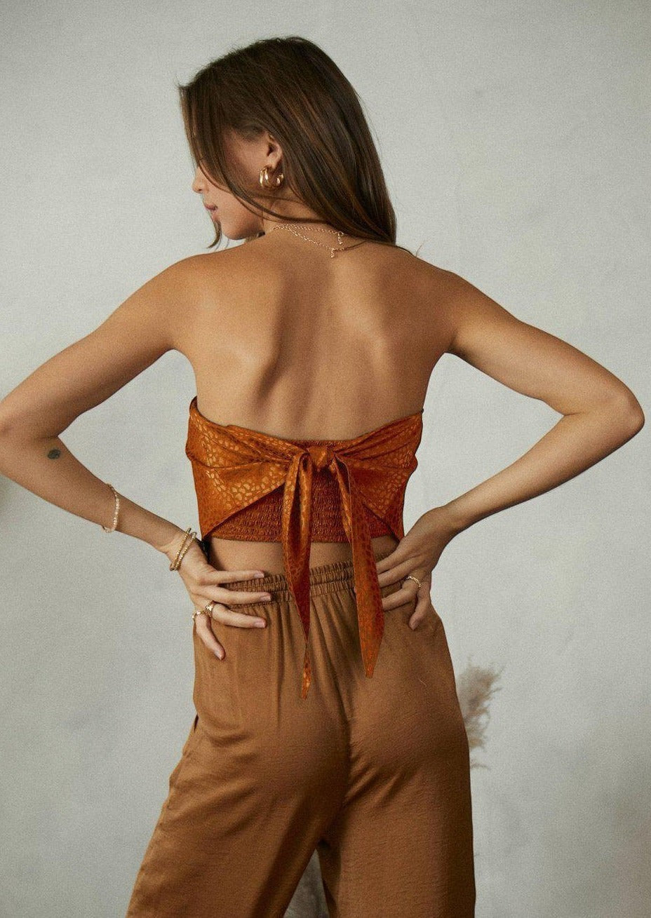 CAL JUNE Tessie satin strapless top with smocked back and a large bow detail in burnt orange.
