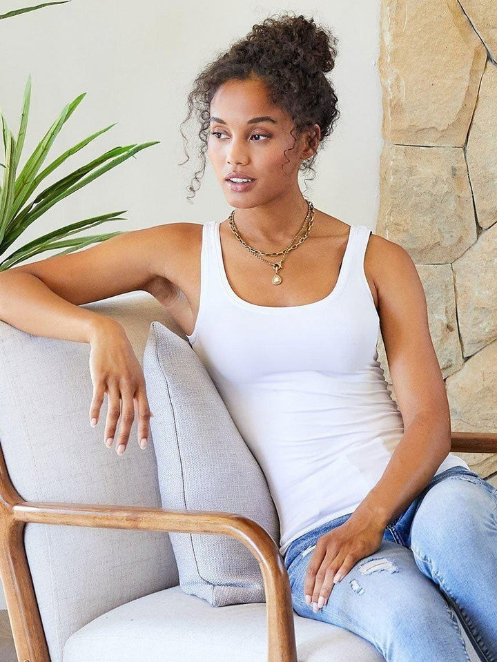 CAL JUNE white scoop neck tank top with a streamlined fit, worn by a model sitting on a chair.