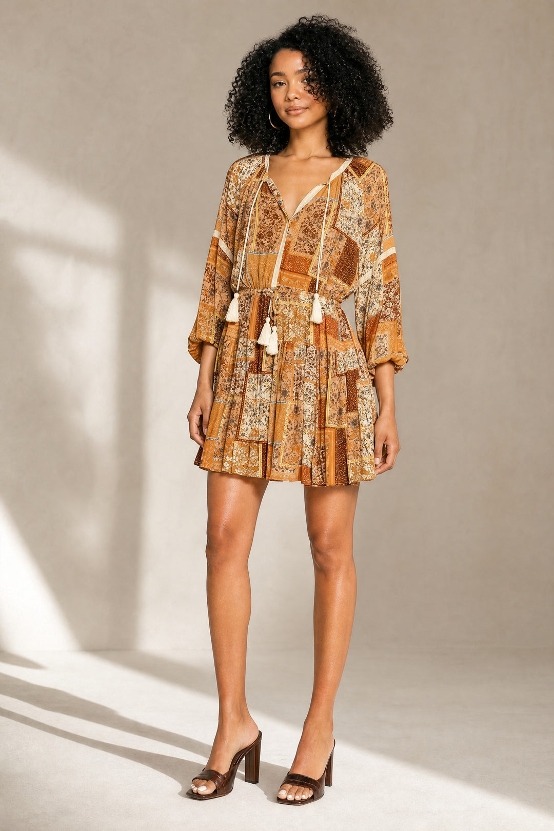 Woman wearing a patterned dress with tassels against a neutral background