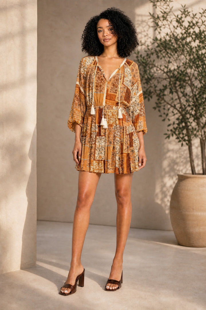 Woman wearing a patterned dress standing in a sunlit room with a plant in the background